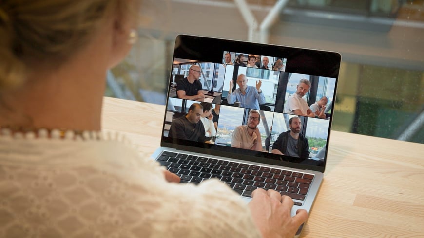 Remote deelnemer ziet een grote vergaderzaal waarin de actieve sprekers groter in beeld staan dan de rest van de tafel